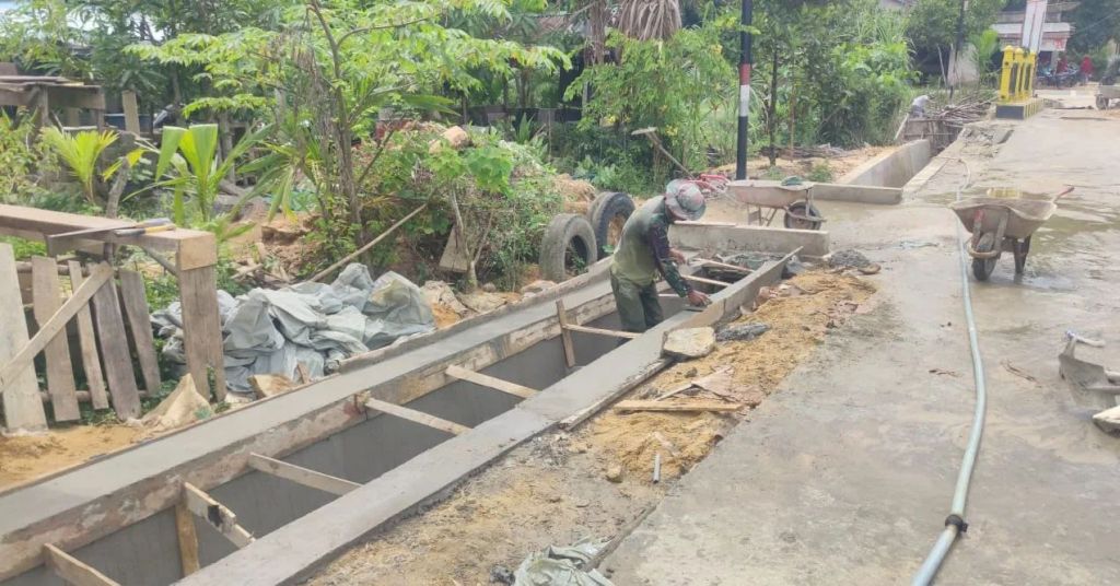 Anggota Satgas TMMD 115 Plester Parit jalan yg telah dibuat